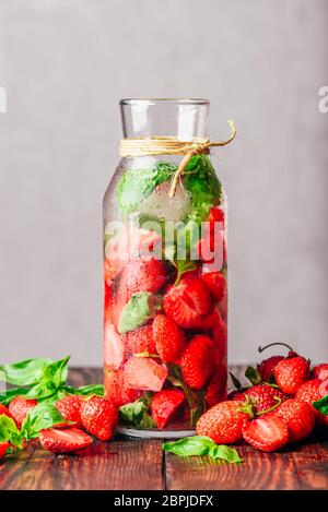 Flasche Wasser hineingegossen mit frischen Erdbeeren und Basilikum. Zerstreut Zutaten auf Holztisch. Vertikale Ausrichtung und Kopieren. Stockfoto