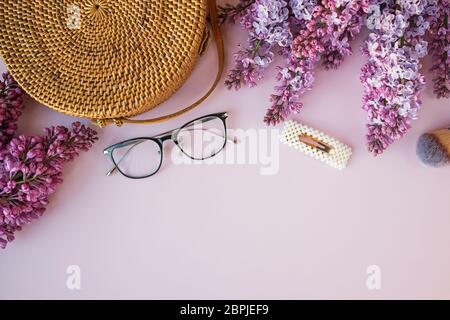 Komposition mit lila lila lila lila Blüten, Handtasche und Brille auf rosa Hintergrund Stockfoto