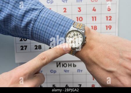 Hand Office Specialist zu einer Armbanduhr, und im Hintergrund ist ein Wandkalender Stockfoto