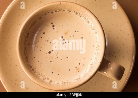 Tasse Kaffee schaumig heißes Getränk auf beigefarbenen Teller auf braunem Hintergrund. Stockfoto