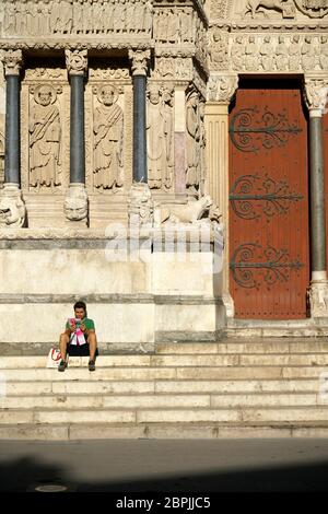 Ein Besucher ruht auf der Treppe unter romanischen Skulpturen schmücken das Portal der Kirche von St.Trophime.Place de la Republique.Arles.France Stockfoto