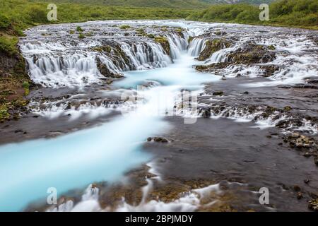 Helle leistungsstarke Bruarfoss Wasserfall in Island mit cyan Wasser verschwommen durch lange Belichtung. Beliebte Touristenattraktion. Ungewöhnliche und malerische Szene. Lo Stockfoto