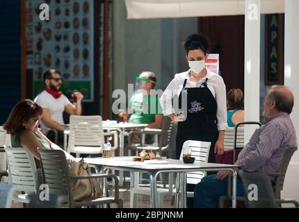 Ein Kellner, der eine Gesichtsmaske trägt, wird während der teilweisen Sperrung im ganzen Land auf der Terrasse einer Bar mit den Kostümen plaudern sehen. Spanien durchläuft einen Plan zur Absenkung hin zu einer "neuen Normalität" durch Lockerung der Maßnahmen, die sich aus dem Ausbruch der COVID-19 ergaben. Während Phase 1 ist erlaubt, dass Menschen ihre Familien besuchen und mit einer Anzahl von maximal 10 Personen in Häusern, im Freien und Terrassen treffen können. Auch können Kirche, Geschäfte, Geschäfte und Bars oder Restaurants mit ihren Terrassen auf 50% begrenzt wieder öffnen, halten Sicherheitsabstand und die Verwendung von Gesichtsmasken. Stockfoto