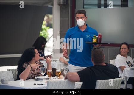 Während der teilweisen Sperrung im ganzen Land wird ein Kellner mit Gesichtsmaske gesehen, der während der teilweisen Sperrung Getränke an die Gäste auf der Terrasse der Strandbar "Gutierrez" serviert. Spanien durchläuft einen Plan zur Absenkung hin zu einer "neuen Normalität" durch Lockerung der Maßnahmen, die sich aus dem Ausbruch der COVID-19 ergaben. Während Phase 1 ist erlaubt, dass Menschen ihre Familien besuchen und mit einer Anzahl von maximal 10 Personen in Häusern, im Freien und Terrassen treffen können. Auch können Kirche, Geschäfte, Geschäfte und Bars oder Restaurants mit ihren Terrassen auf 50% begrenzt wieder öffnen, halten Sicherheitsabstand und die Verwendung von Gesichtsmasken. Stockfoto