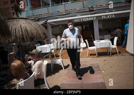 Während der teilweisen Sperrung im ganzen Land wird ein Kellner mit Gesichtsmaske gesehen, der während der teilweisen Sperrung auf der Terrasse der Strandbar "Gutierrez" ein Bier an die Gäste serviert. Spanien durchläuft einen Plan zur Absenkung hin zu einer "neuen Normalität" durch Lockerung der Maßnahmen, die sich aus dem Ausbruch der COVID-19 ergaben. Während Phase 1 ist erlaubt, dass Menschen ihre Familien besuchen und mit einer Anzahl von maximal 10 Personen in Häusern, im Freien und Terrassen treffen können. Auch können Kirche, Geschäfte, Geschäfte und Bars oder Restaurants mit ihren Terrassen auf 50% begrenzt wieder öffnen, halten Sicherheitsabstand und die Verwendung von Gesichtsmasken. Stockfoto