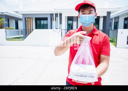 Asiatische Lieferung Soldaten tragen eine rote Uniform mit einer roten Kappe und Gesichtsmaske Umgang Lebensmittelboxen in Plastiktüten, um den Kunden vor t zu geben Stockfoto