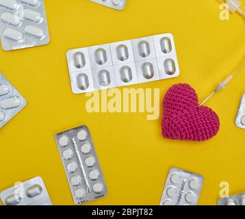 Rotes Herz und Katheter auf gelbem Hintergrund in der Mitte der Pakete mit weißen Tabletten, full frame Stockfoto