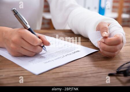 Nahaufnahme der Geschäftsfrau mit weißen Bandagen Hand Befüllen Arbeitsunfall Antragsformular auf hölzernen Schreibtisch Stockfoto