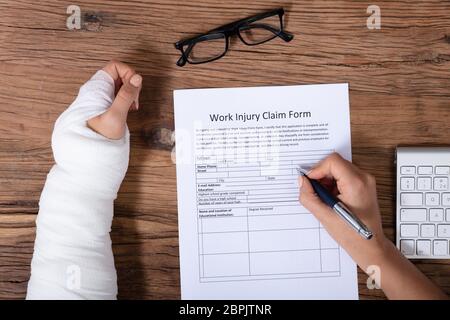 Nahaufnahme der Geschäftsfrau mit weißen Bandagen Hand Befüllen Krankenversicherung Antragsformular auf hölzernen Schreibtisch Stockfoto