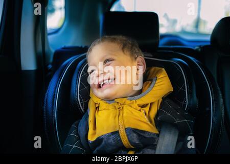 Ein fröhlicher kleiner Junge lächelt auf dem Kindersitz. Sicherheit von Kindern beim Fahren Stockfoto