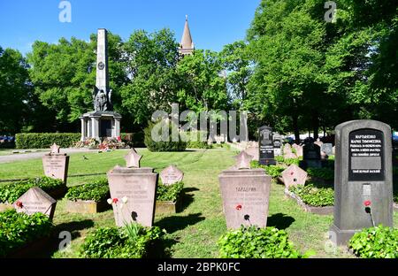 12. Mai 2020, Brandenburg, Potsdam: Das Denkmal auf dem sowjetischen Ehrenfriedhof am Bassinplatz, im Hintergrund hinter Bäumen die Spitze der katholischen Pfarrkirche St. Peter und Paul zu sehen. Etwa 400 Gräber und ein mit Bronzefiguren geschmückter Obelisk erinnern an gefallene Soldaten der sowjetischen Armee während der Schlacht von Berlin. Die Soldaten der Roten Armee, die auf dem Sockel des Sandstein-Granit-Denkmals stehen, stellen die vier Zweige der Armee durch einen Wachsoldaten, einen Panzerfahrer, einen Marineinfanteristen und einen Piloten dar. Der Ehrenfriedhof steht seit 1987 unter Denkmalschutz. Stockfoto