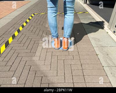 Nahaufnahme von isolierten Schuhen und Beinen einer Person auf blauem Markierungsschild auf dem Boden, die beim Anstehen am Eingang des Shops warten und Abstand halten Stockfoto