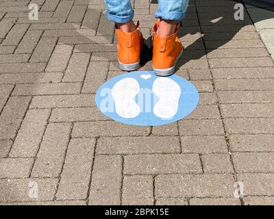 Nahaufnahme von isolierten Schuhen und Beinen einer Person auf blauem Markierungsschild auf dem Boden warten und halten Abstand, während am Eingang des Geschäfts in CO Schlange stehen Stockfoto