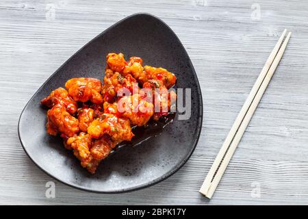 Koreanische, Chinesische Küche - Ansicht von oben Kkanpunggi scharf gebratenes Huhn mit Gemüse in süß-saurer Soße auf schwarze Platte mit Essstäbchen auf g Stockfoto