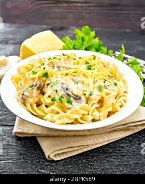 Fusilli mit Champignons in Rahmsauce, Petersilie und geriebenem Käse in einer Platte auf Serviette auf dem Schwarzen Brett Hintergrund Stockfoto