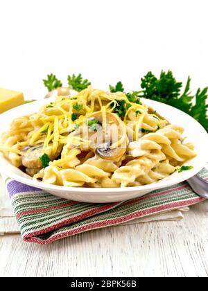 Fusilli mit Champignons in Rahmsauce, Petersilie und geriebenem Käse in einer Schüssel auf Küchenpapier gegen Licht Holzbrett Stockfoto