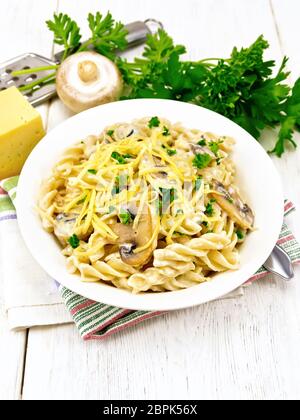 Fusilli mit Champignons in Rahmsauce, Petersilie und geriebenem Käse in einer Schüssel auf Küchenpapier gegen Licht Holzbrett Stockfoto