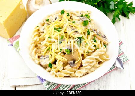 Fusilli mit Champignons in Rahmsauce, Petersilie und geriebenem Käse in eine Platte auf dem Handtuch gegen Licht Holzbrett Stockfoto