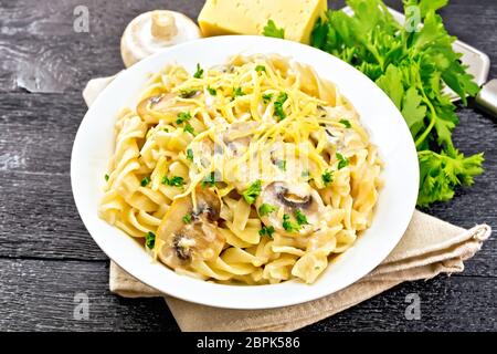 Fusilli mit Champignons in Rahmsauce, Petersilie und geriebenem Käse in einer Platte auf Serviette auf Holzbrett Hintergrund Stockfoto