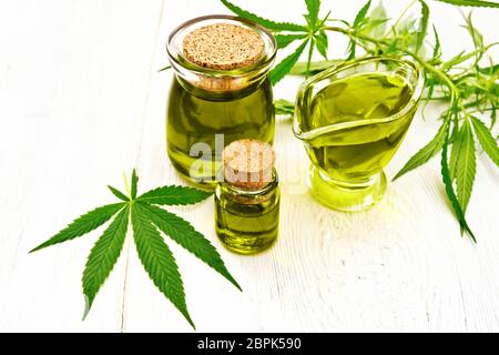 Hanf Öl in zwei Gläsern und sauceboat, Blätter und Stängel von Cannabis vor dem Hintergrund der weißen Brettern Stockfoto