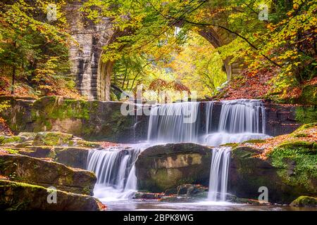 Herbsttag im sonnigen Wald. Alte Steinbrücke. Kleiner Fluss und mehrere natürliche Wasserfälle Stockfoto