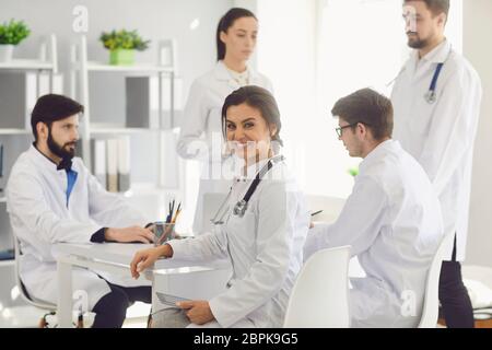 Ärztin sitzt an einem Tisch mit Kollegen in weißen Labormänteln in einem medizinischen Krankenhaus. Stockfoto