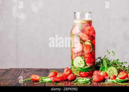 Flasche Wasser gewürzt mit frischen Erdbeeren, in Scheiben geschnittene Gurken und Federn von Thymian. Zutaten verstreut auf Holztisch. Kopieren Sie Platz. Stockfoto