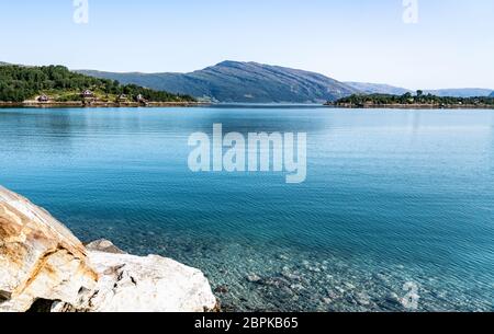 Blick auf die ruhige Bucht in Norwegen, nahe Sandnessjoen Stadt, blaues Wasser des Atlantiks, Berge am Horizont, norwegische Häuser und Blick aus der Nähe bei großen sto Stockfoto