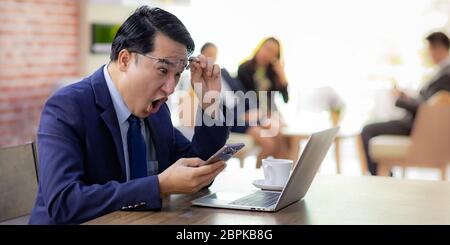 Portrait von Asiatische Geschäftsmann feiern und froh für seinen Erfolg im Cafe mit Smartphone und Laptop mit Business Team im Hintergrund für copor Stockfoto