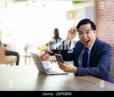 Portrait von Asiatische Geschäftsmann feiern und froh für seinen Erfolg im Cafe mit Smartphone und Laptop mit Business Team im Hintergrund für copor Stockfoto