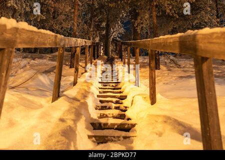 Rutschige Holztreppe im Kiefernwald voll mit Schnee bedeckt. Winterwunderland. Treppen steigen. Lappland, Nordschweden Stockfoto