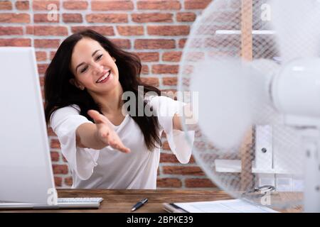 Gerne Reife Geschäftsfrau kühlen sich mit elektrischen Lüfter am Arbeitsplatz am Schreibtisch aus Holz Stockfoto