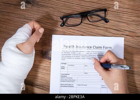 Nahaufnahme der Geschäftsfrau mit weißen Bandagen Hand Befüllen Krankenversicherung Antragsformular auf hölzernen Schreibtisch Stockfoto