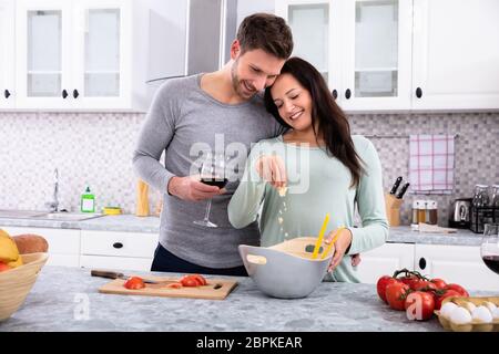 Lächelnde Frau Besprühen die Butter, die mit ihrem Mann in der Küche Holding Wein Glas Stockfoto