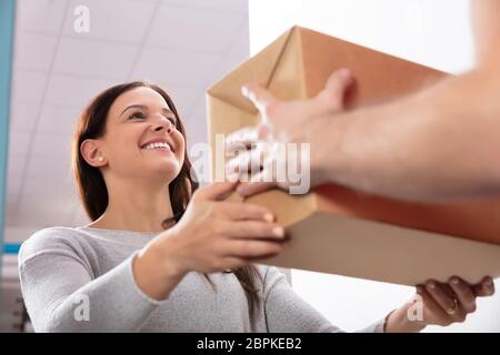 Glückliche junge Frau akzeptieren Karton ab Lieferung Mann Stockfoto