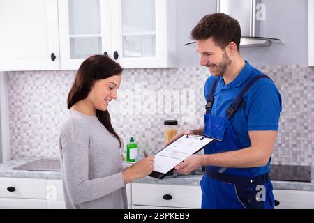Glückliche junge männliche Klempner bei Frau Unterzeichnung Rechnung in der Küche Stockfoto