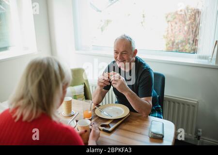 Älterer Mann lacht und spricht mit seinem Partner, während sie das Frühstück gemeinsam zu Hause genießen. Stockfoto