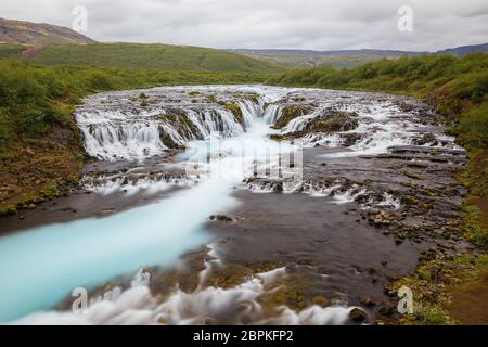 Helle leistungsstarke Bruarfoss Wasserfall in Island mit cyan Wasser verschwommen durch lange Belichtung. Beliebte Touristenattraktion. Ungewöhnliche und malerische Szene. Lo Stockfoto