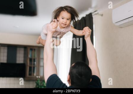 Vater wirft seine geliebte lachende Tochter im Wohnzimmer auf. Stockfoto