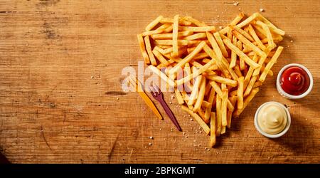 In Herzform dienen oder frittierten Kartoffelchips, Pommes frites oder Pommes frites auf rustikalem Holz mit Senf und Mayonnaise mischen und Tomatensauce vie Stockfoto