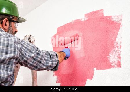 Kaukasische Haus Maler Arbeiter auf einem metallischen Leiter, mit der Walze er malt die Wand mit den farbigen Anstrich von Pink. Bauindustrie. Unten Stockfoto