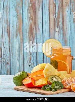 Fruchtlimonade mit Eis, Minzblättern, Zitrone, Ananas, Mango und Limettenscheiben stehen auf blauem Holztisch. Hausgemachte Limonade mit gemischten Früchten. Hea Stockfoto