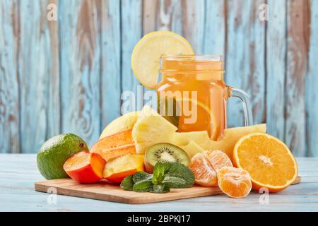 Fruchtlimonade mit Eis, Minzblättern, Zitrone, Ananas, Mango und Limettenscheiben stehen auf blauem Holztisch. Hausgemachte Limonade mit gemischten Früchten. Hea Stockfoto