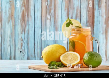 Zitruslimonade mit Eis, Minzblättern, Zitronen- und Limettenscheiben stehen auf einem blauen Holztisch. Hausgemachte Limonade mit Zitrusfrüchten. Gesundes kühles Getränk Stockfoto