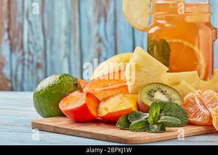 Fruchtlimonade mit Eis, Minzblättern, Zitrone, Ananas, Mango und Limettenscheiben stehen auf blauem Holztisch. Hausgemachte Limonade mit gemischten Früchten. Hea Stockfoto