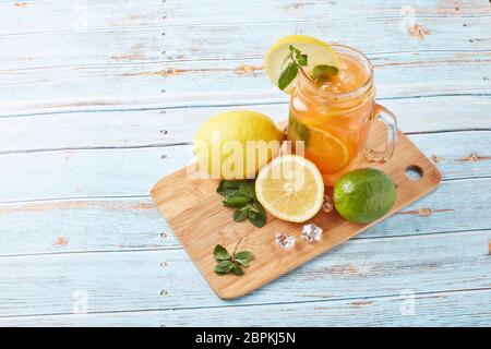 Zitruslimonade mit Eis, Minzblättern, Zitronen- und Limettenscheiben stehen auf einem blauen Holztisch. Hausgemachte Limonade mit Zitrusfrüchten. Gesundes kühles Getränk Stockfoto