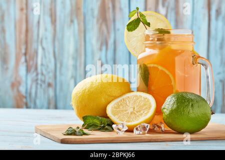 Zitruslimonade mit Eis, Minzblättern, Zitronen- und Limettenscheiben stehen auf einem blauen Holztisch. Hausgemachte Limonade mit Zitrusfrüchten. Gesundes kühles Getränk Stockfoto