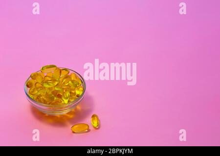 Gelb transparent Kapseln mit Fischöl, Omega-3-Säuren in einem transparenten Schale auf einem rosa Hintergrund. Stockfoto