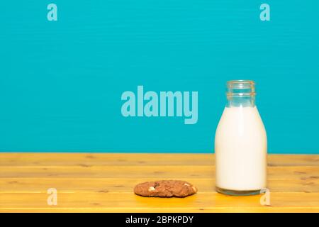 Frische, cremige Milch in einem Drittel pint Glas Milch-Flasche und einen Chocolate Chip Cookie, auf einen hölzernen Tisch gegen einen hellen Teal gemalten Hintergrund Stockfoto