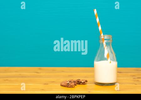 Ein Drittel pint Glas Milch Flasche halb voll mit frischen Cremige Milch mit retro Stroh und ein halbes gegessen Chocolate Chip Cookie, auf einen hölzernen Tisch gegen Stockfoto
